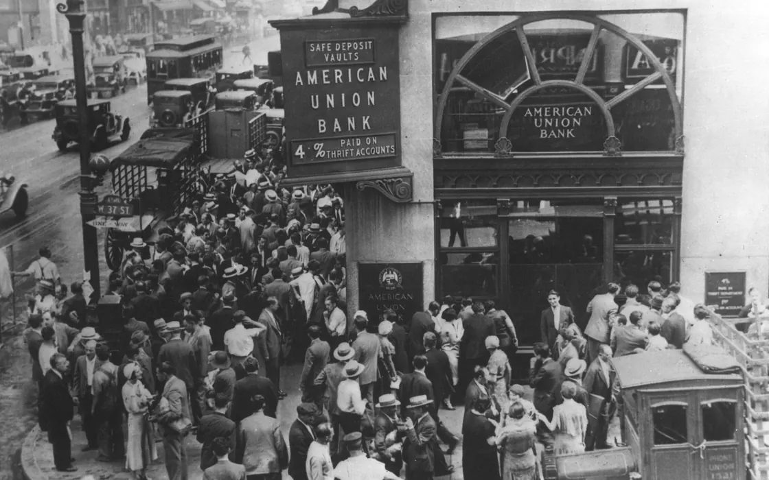 Fotografia de 26 de abril de 1932: multidão de depositantes aglomerada na calçada diante do American Union Bank fechado, em Nova York, sob uma placa que anuncia 4% pagos em contas de poupança