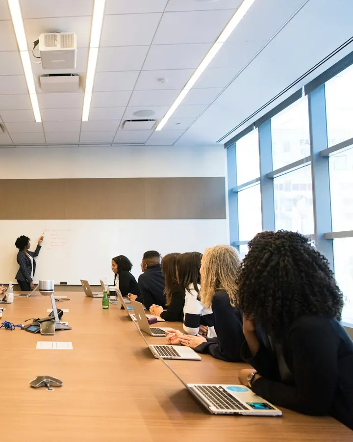 Pessoas sentadas em volta de uma mesa de reunião, olhando para quem apresenta