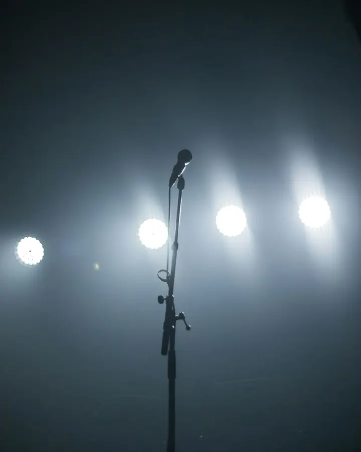 Microfone sozinho num palco vazio, iluminado por quatro refletores ao fundo