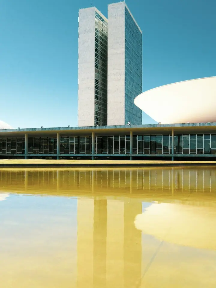 Congresso Nacional, em Brasília, refletido no espelho d'água sob céu azul.